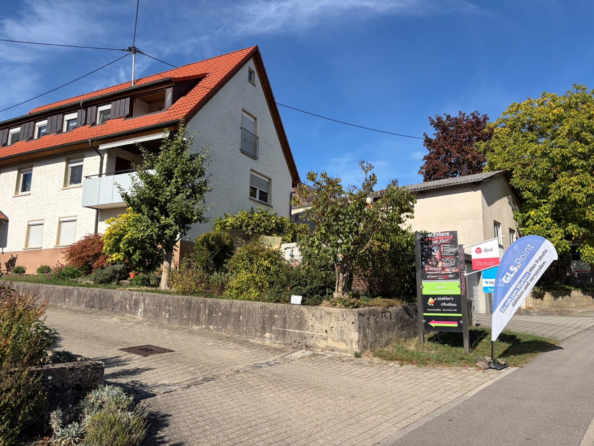 Blick von der Straße auf die beschilderte Einfahrt von Alessios Rollerservice in Zweiflingen